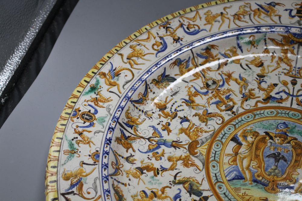 A 19th century Italian 17th century style maiolica charger, decorated with cherubs flanking a cartouche within bands of stylised beasts